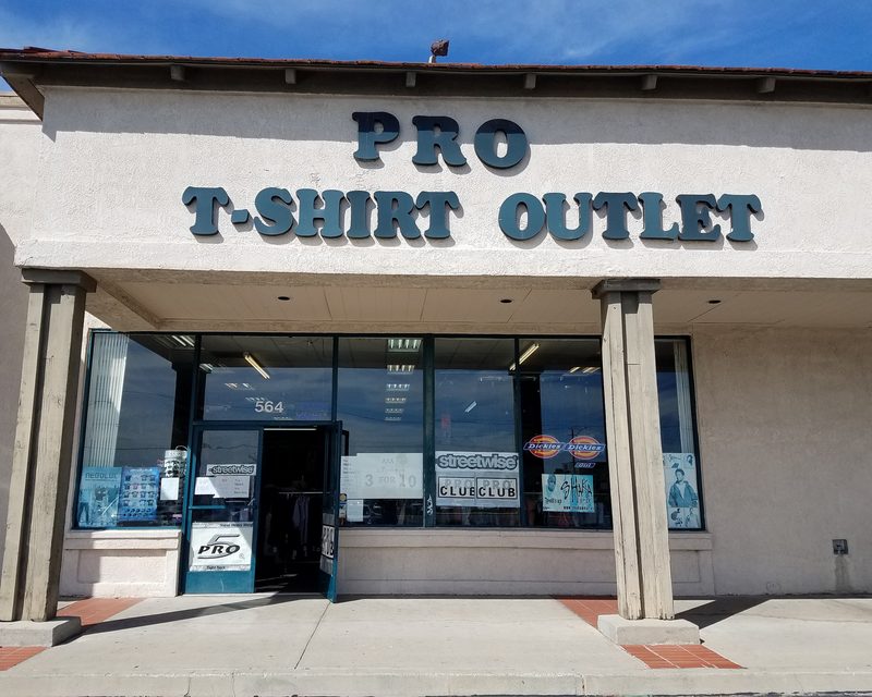 Pro T-Shirt Outlet storefront in Rialto. The sign is large black dimensional letters, faded by the sun, on stucco.